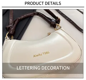 Close-up of a beige crescent bag with Aiwitu'1986 gold lettering and brown ruched handle