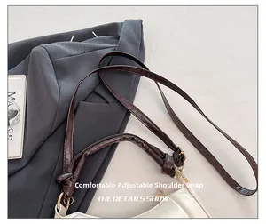 Detail view of adjustable brown leather shoulder strap with golden buckle on white crescent bag