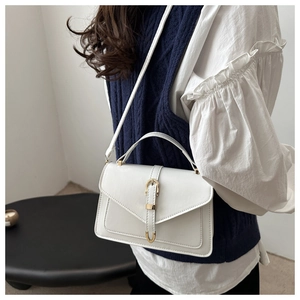 Zijaanzicht van witte crossbodytas met gouden gesp op een blauw vest en blouse