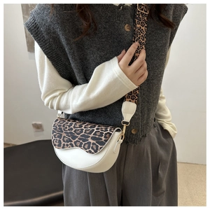 Close-up of white faux leather saddle bag with leopard print flap and wide shoulder strap