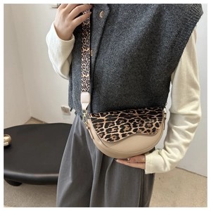 Close-up of leopard print saddle bag with wide strap worn by a model in soft light