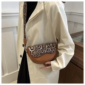 Detail of saddle bag with leopard print strap worn by model over a white trench coat