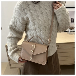 Detail van beige crossbodytas met gouden gesp gedragen op een zachte gebreide trui