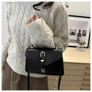 Detail van elegante zwarte lederen crossbodytas met gouden gesp op gebreide trui achtergrond