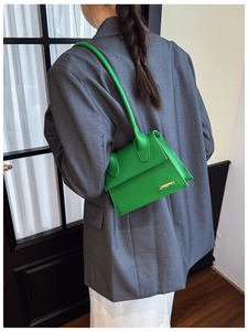 Close-up of vibrant green leather handbag with metal logo and unique long handle