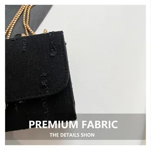 Close-up of black denim fabric texture and golden snake chain on woman small square bag
