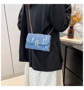 Detail of blue denim crossbody bag with gold chain strap and distressed vintage finish