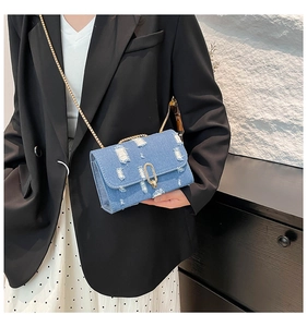 Detail of light blue denim crossbody bag with gold chain strap and distressed fabric texture
