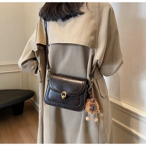 Detail of dark brown leather crossbody bag with gold twist lock and a cute bear charm