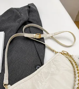 Detail van witte leren schoudertas met verstelbare riem en gouden kettingaccent