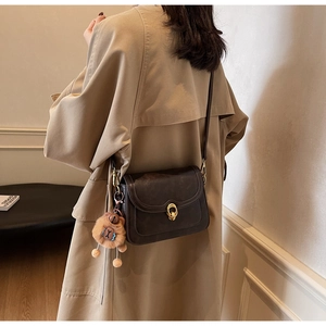 Detailed side view of dark brown faux leather crossbody bag with a plush bear charm