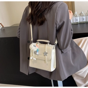 Detail of cream white crossbody bag with silver star buckle and plush charm on the strap