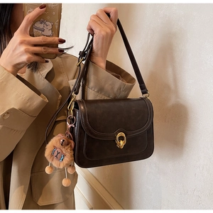 Close-up of vintage brown PU leather crossbody bag with gold clasp and plush charm