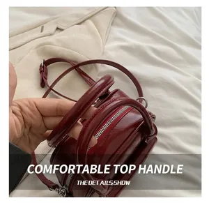 Detail of wine red patent leather handbag with round handle and dual zipper closure