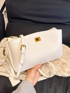 White leather handbag with gold metal lock and adjustable strap held in hand
