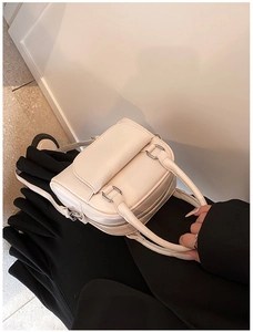 Detail of cream leather handbag with glossy finish, dual zippers, and silver hardware accents