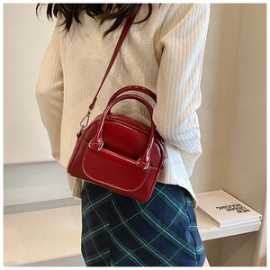 Detail of dark red patent leather handbag with glossy finish and detachable shoulder strap