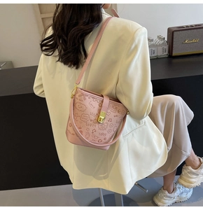 Pink bucket bag with cartoon graffiti print and metal lock shown on shoulder