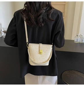 Detail of cream bucket bag with embossed graffiti pattern and golden swivel lock closure