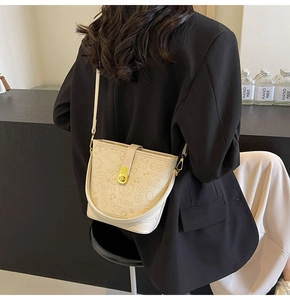 Detail of cream white bucket bag with embossed lettering and golden twist lock