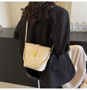 Detailed view of white bucket bag featuring embossed heart patterns and gold metal twist lock