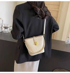 Detailed view of the creamy white bucket bag with graffiti embossing and gold metal lock