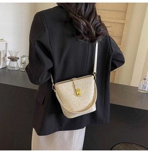Detail of beige bucket bag with embossed lettering, metal lock and leather strap on a model