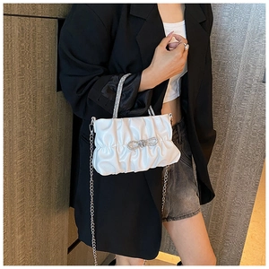 Detail of white pleated handbag with rhinestone bow and silver chain on black blazer