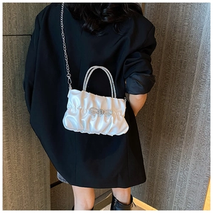 Close-up of white pleated evening bag with rhinestone bow and chain strap on a black blazer