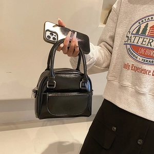 Minimalist black patent leather handbag with dual handles and glossy finish shown held by hand