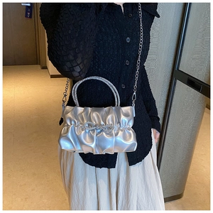 Detail of silver pleated handbag with rhinestone bow buckle and shiny metallic finish