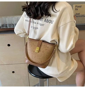 Brown leather bucket bag with graffiti embossing and adjustable strap on a model
