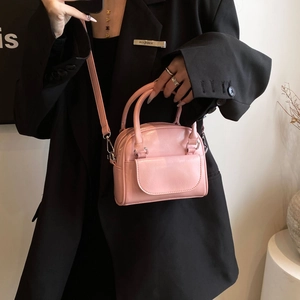 Pink glossy patent leather crossbody bag with round handle and detachable strap on black suit