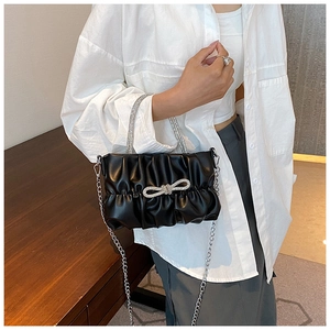 Close-up of black ruched cloud bag featuring a sparkling rhinestone bow and silver chain strap