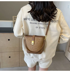 Close-up of brown embossed bucket bag with gold lock and cartoon patterns for women