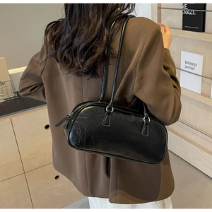 Detailed view of black pleated faux leather shoulder bag worn by model in chic interior
