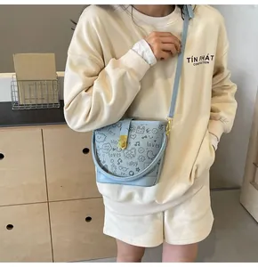 Detail of light blue bucket bag with graffiti prints and metal lock on a crossbody strap