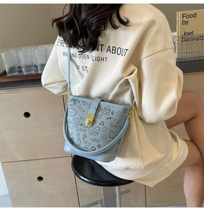 Light blue bucket bag with cartoon graffiti and gold lock shown in a casual lifestyle setting