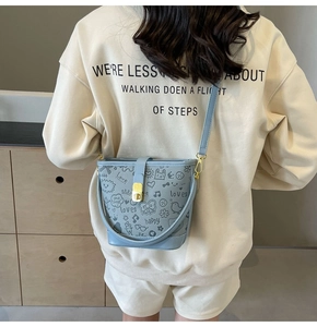Close-up of light blue bucket bag with black graffiti prints and gold metal clasp detail