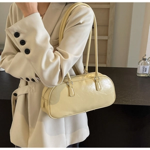 Close-up of a cream-colored pleated faux leather shoulder bag worn by a model