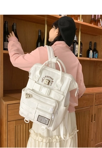 Detail of white multi-pocket backpack showing functional zippers and side bottle pocket