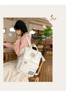 Cream canvas backpack with multi-pockets and bread mascot shown in a cafe setting