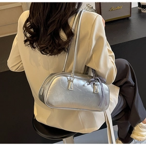 Detail of silver metallic barrel bag with plaid bow ribbon held by a model