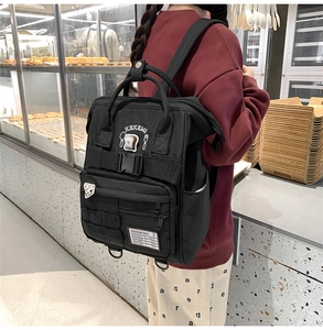 Close-up of black canvas backpack featuring embroidered patches and a functional side pocket