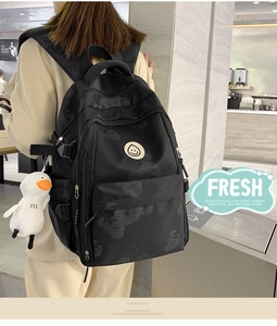 Detail of black printed backpack with bear pattern and a white duck plush pendant