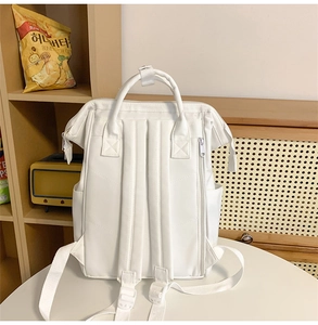 Minimalist white backpack detail showing waterproof fabric in a cozy indoor setting