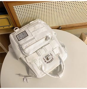 Detail of white multi-pocket canvas backpack featuring functional straps and logo