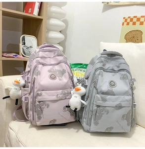 Detail of student backpacks with bear prints and cute duck charms on a white sofa