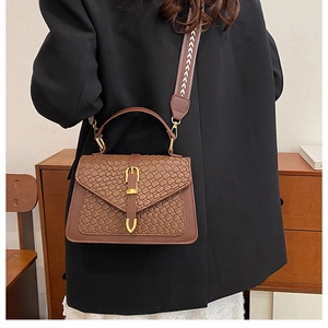 Detail of a brown woven crossbody bag featuring a vintage gold buckle and jacquard strap