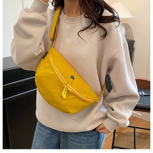 Detalle de bandolera de nailon amarillo con doble cremallera y tiradores de goma